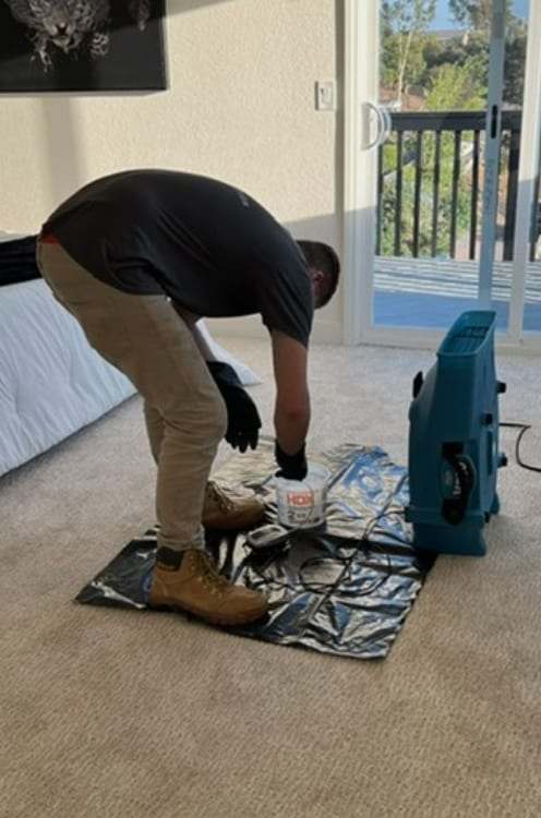 Technician setting an air mover on plastic sheeting in a bedroom